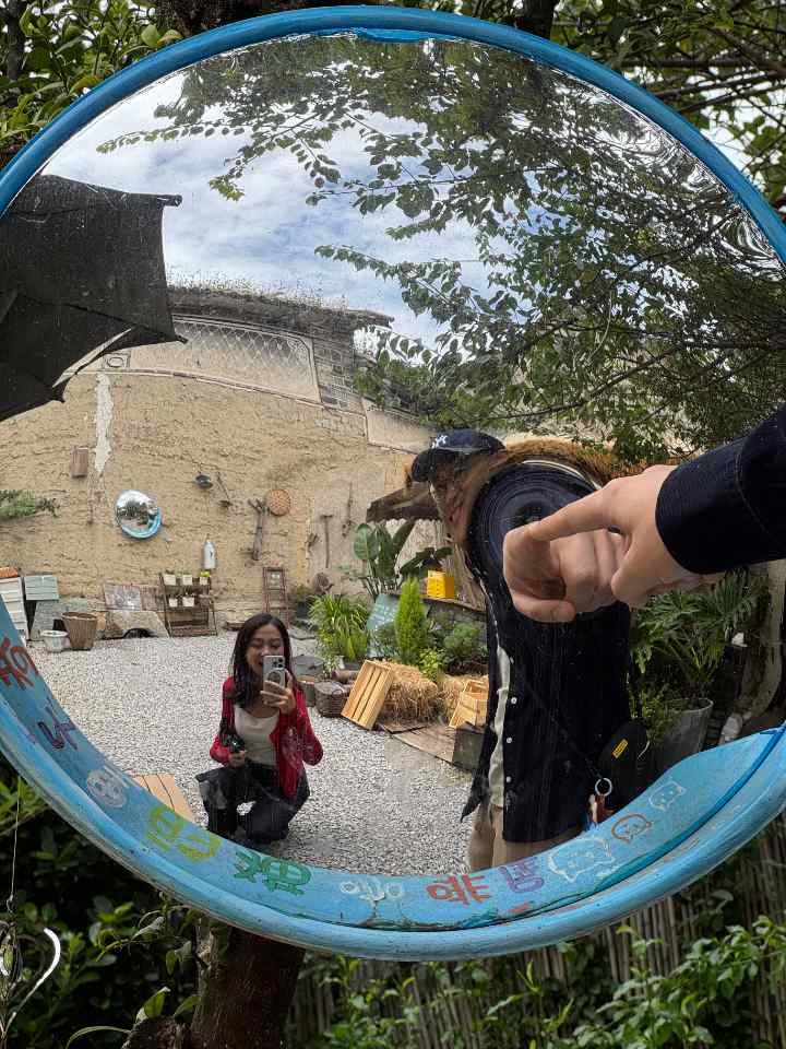 庭院圆镜里映出两人:一人蹲着拍照,一人向镜中伸手
