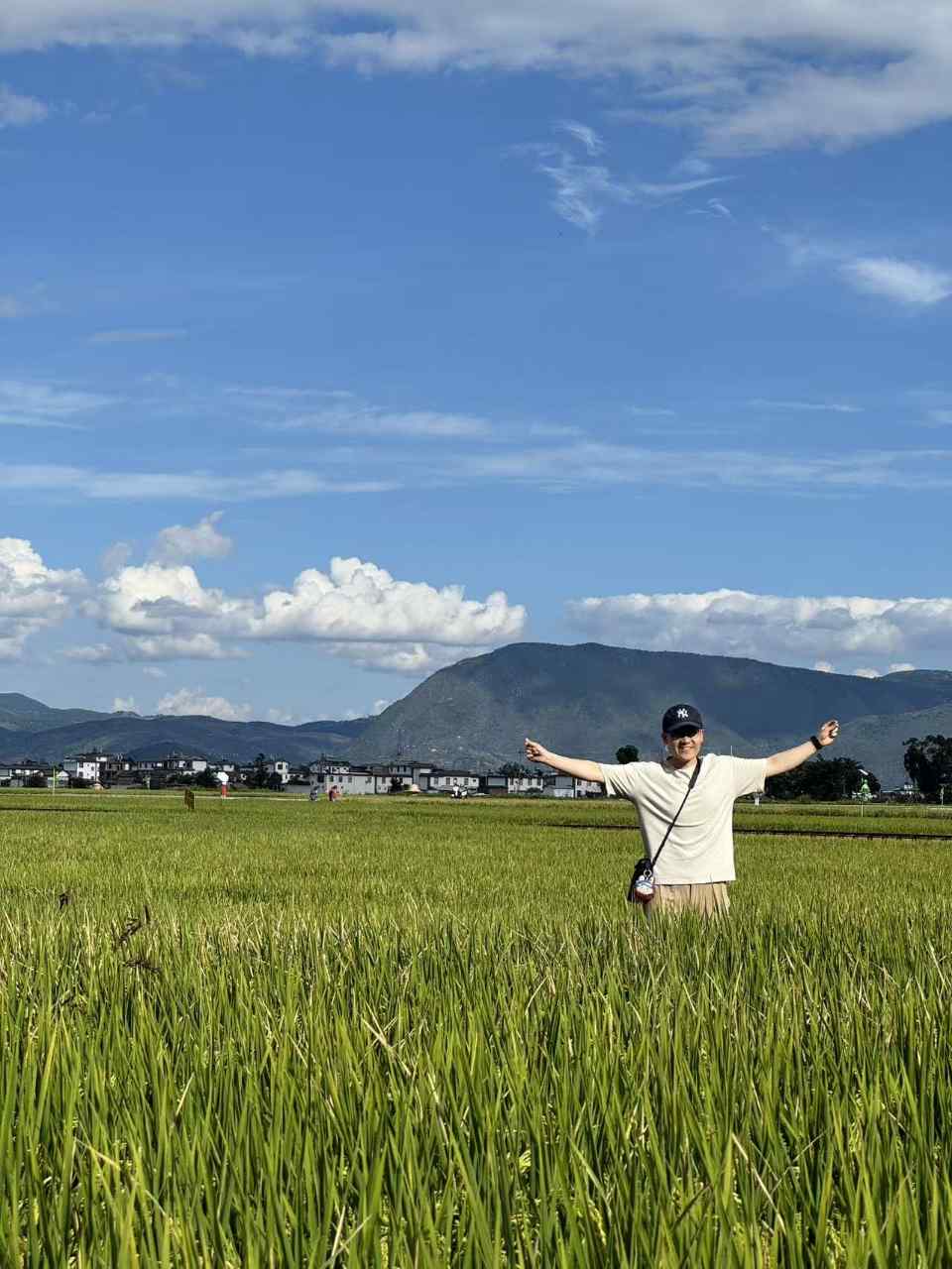 男生在稻田里张开双臂,身后是苍山与村庄