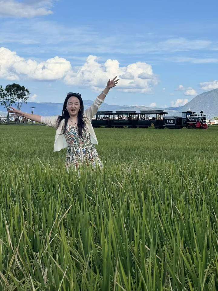 穿碎花裙的女生在稻田中张开双臂,身后一列小火车正缓缓驶过