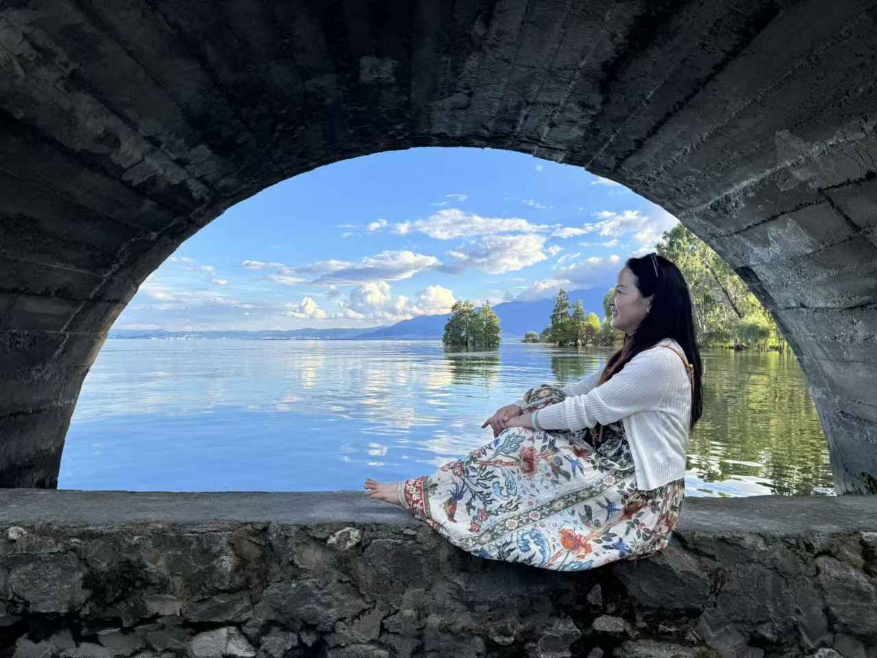 花裙女士坐在桥栏上侧身望着湖面