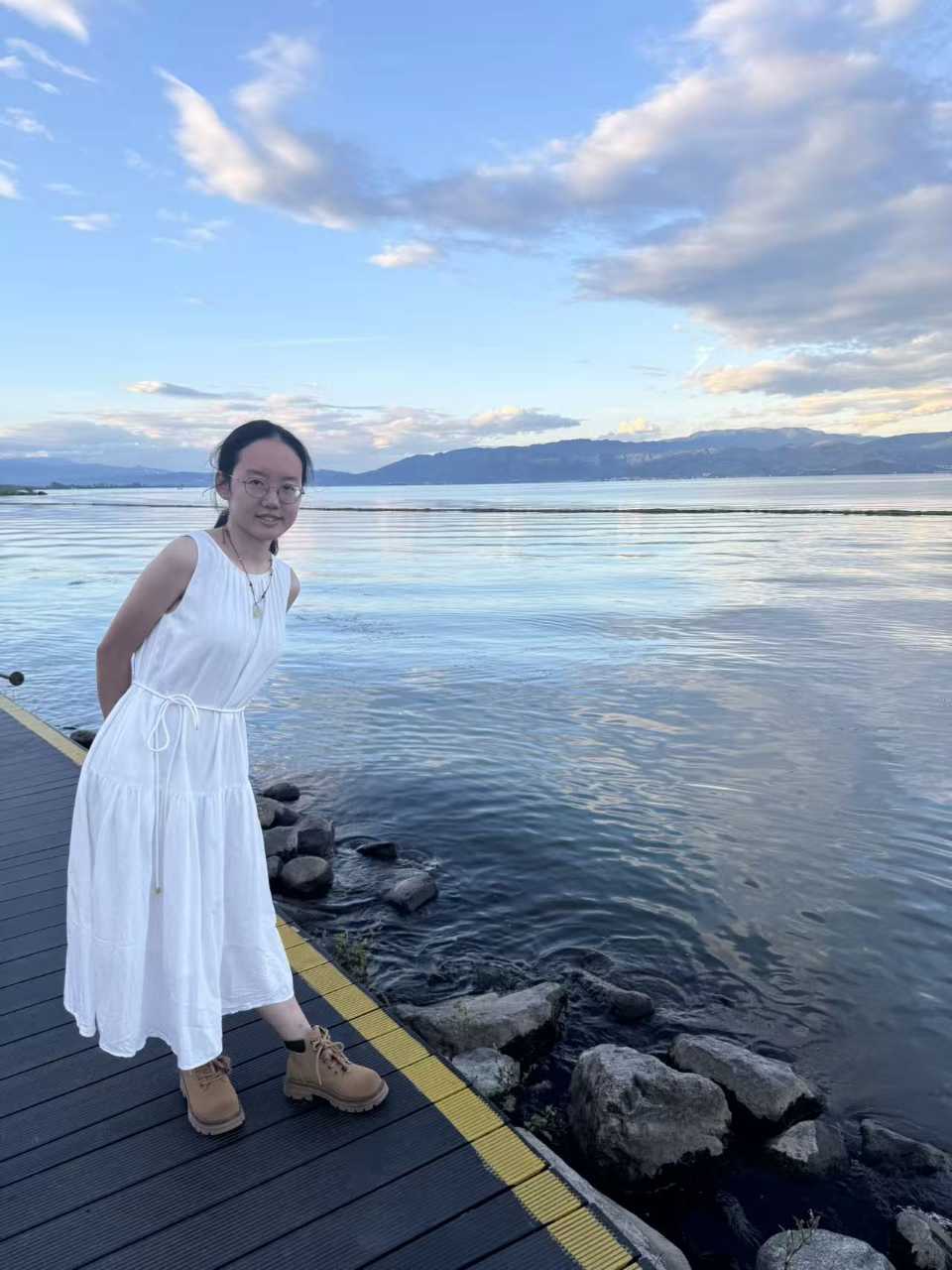 白裙女生站在木栈道上回望,黄昏的洱海与远山