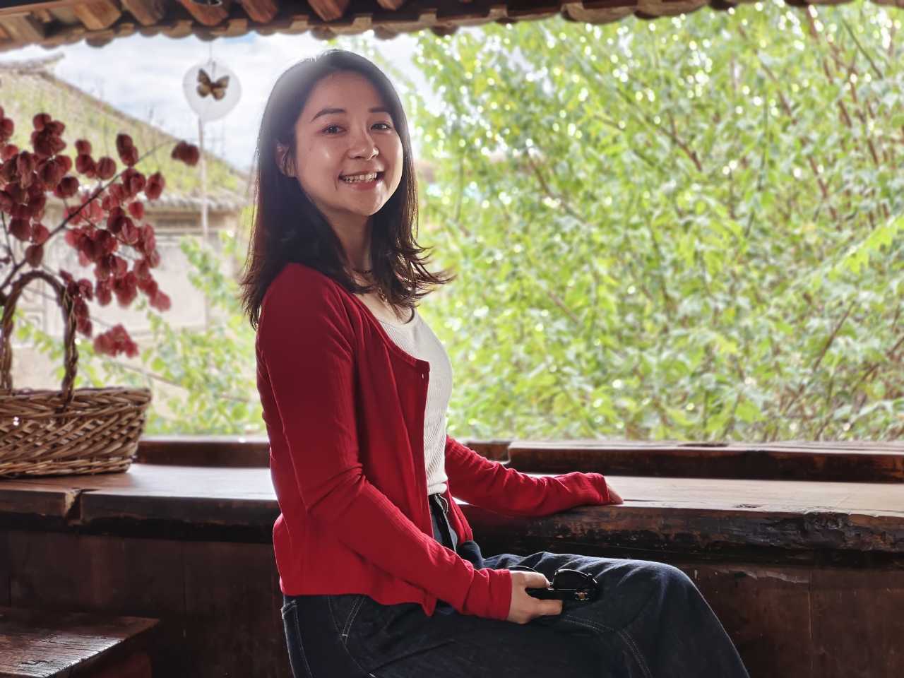 穿红开衫的女生坐在窗边木台上笑着看向镜头